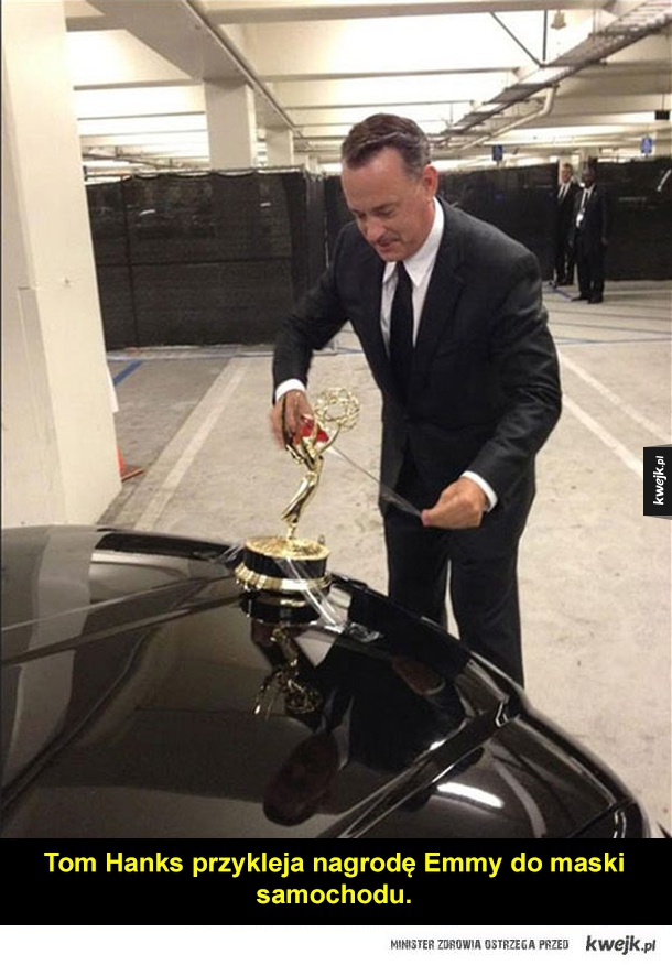 Tom Hanks przykleja nagrodę Emmy do maski samochodu.